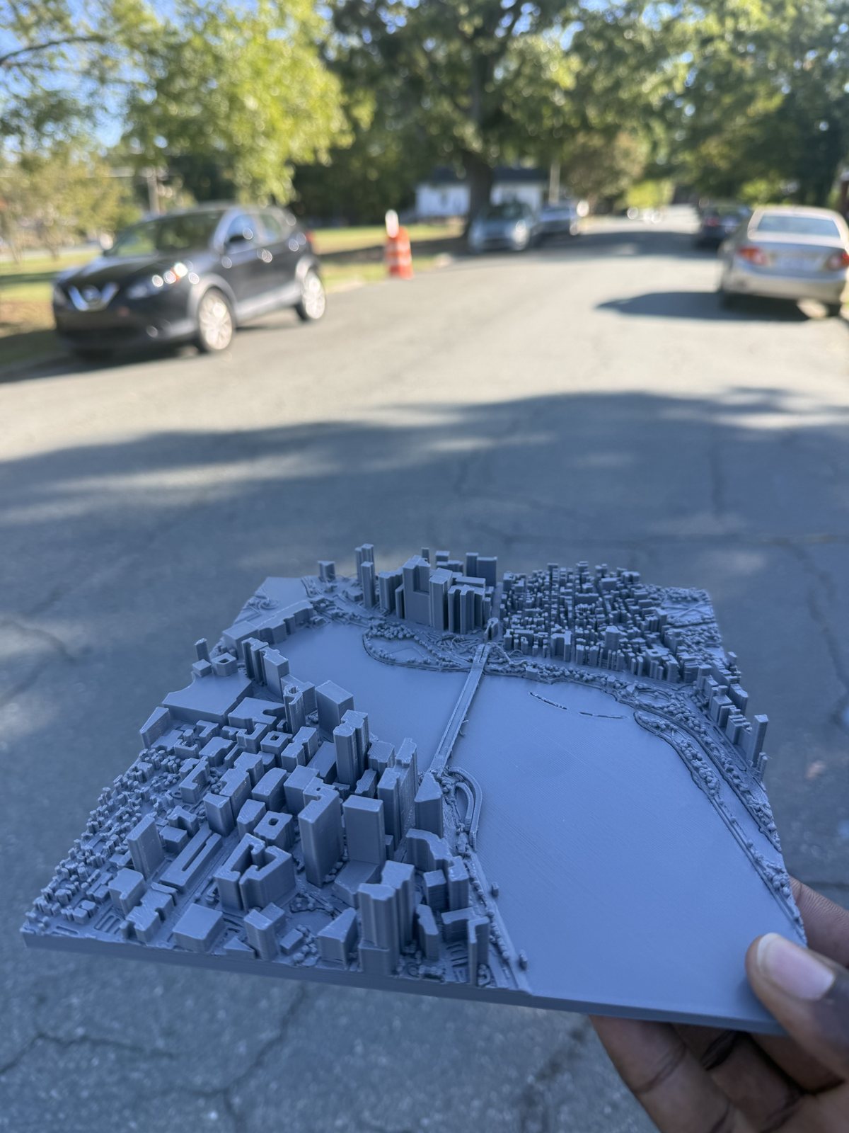 A 3D-printed map of Boston's Charles River and Longfellow Bridge, held up outdoors.